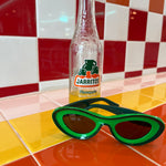 Green sunglasses next to a Jarritos bottle