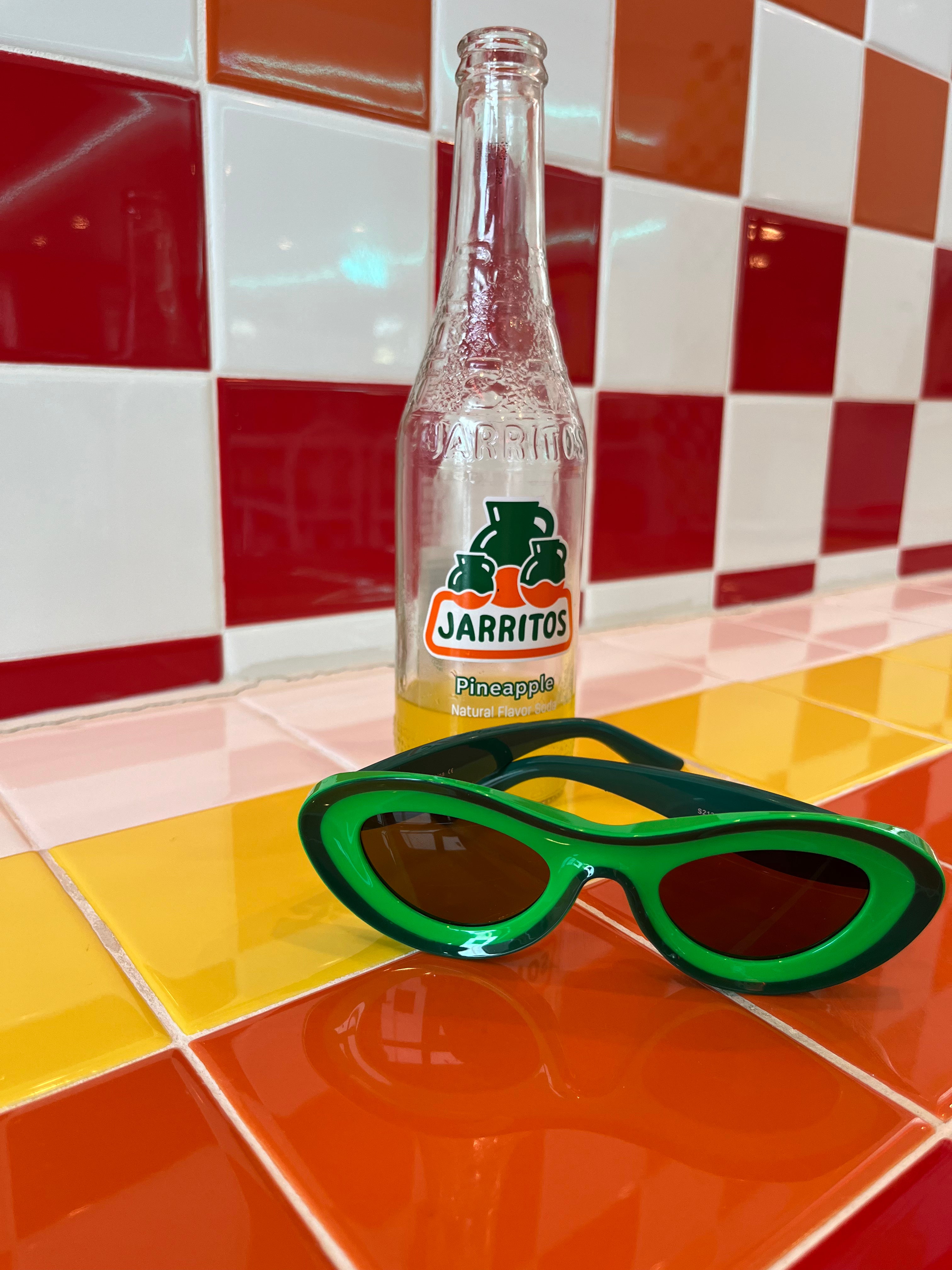 Green sunglasses next to a Jarritos bottle